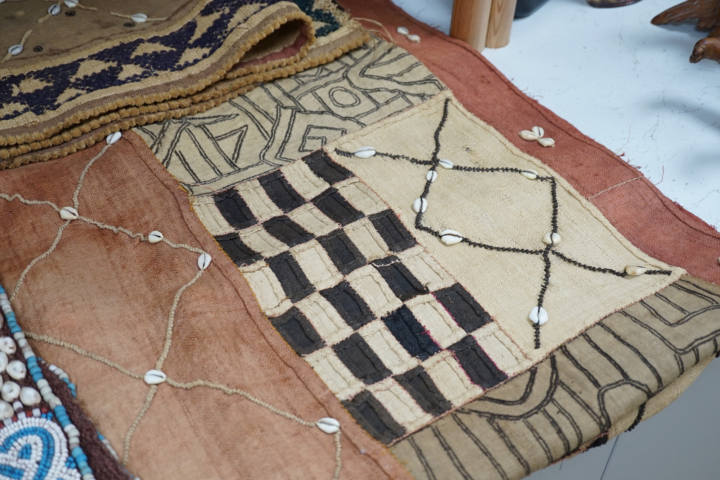 Three African tribal hangings, embroidered with coloured hand dyed threads and appliquéd shells on smaller handwoven cloth panels all sewn together to form the hangings, including a chieftains coloured bead worked and sh